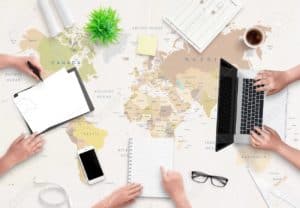 Two people working at a desk with a laptop and notepad on top of a world map