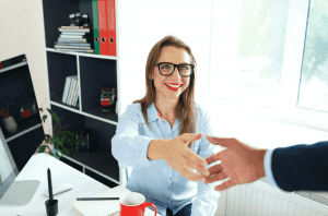 Two businesspeople shaking hands and looking at a document on a desk, with legal books and a pen in the background