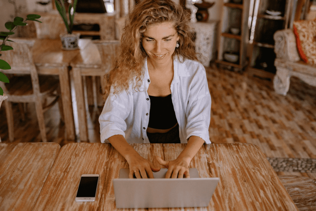 A woman sitting at her computer, smiling while looking at the screen, representing a business owner managing her registered agent service renewal through BusinessAnywhere's online portal.
