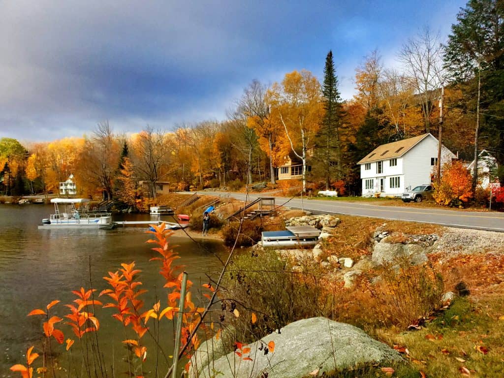 Serene lakeside scene with a white house and picket fence, representing the tranquility of conducting a New Hampshire business entity search.