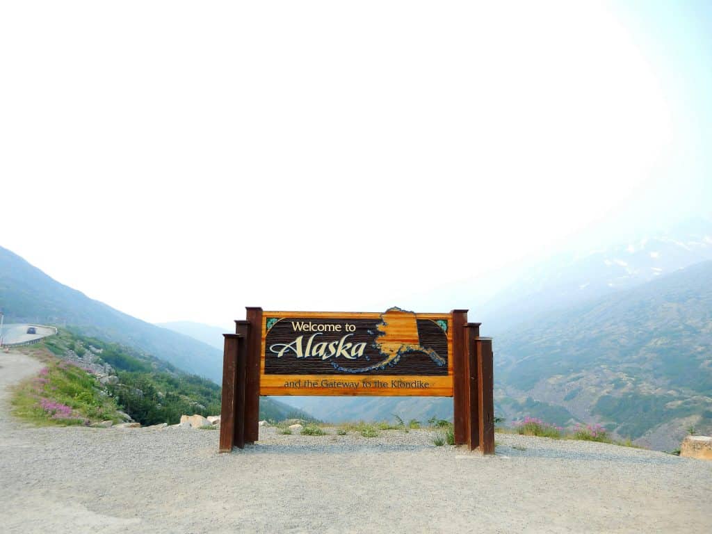 "Welcome to Alaska" sign with snow-capped mountains in the background, representing the concept of an Alaska Business Entity Search​