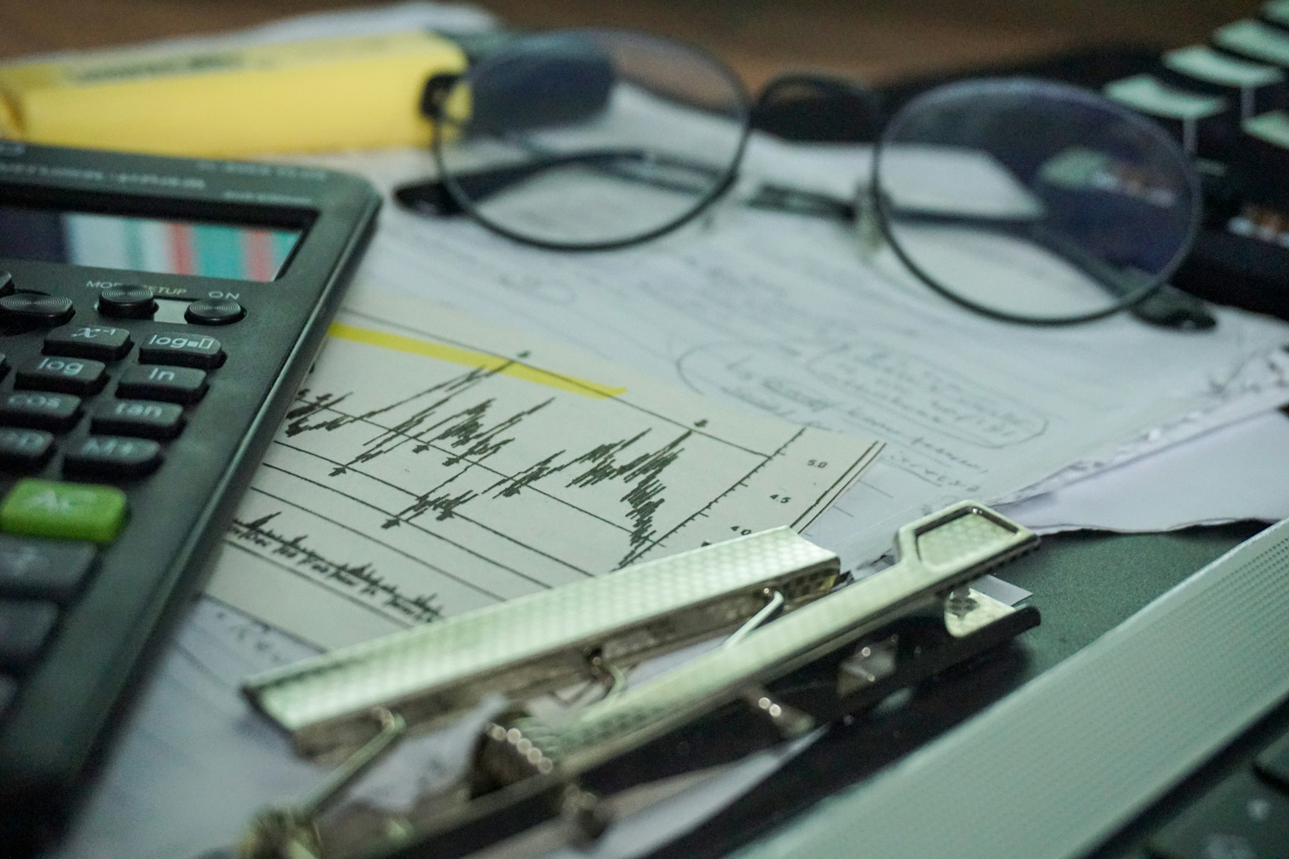 Calculator, eyeglasses and financial paperwork with a price chart on a desk