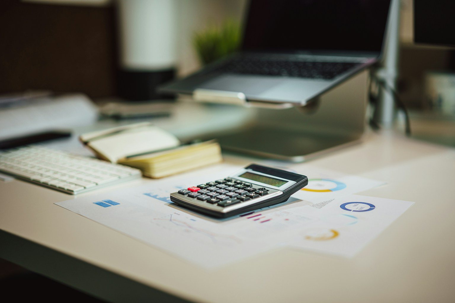 Calculator resting on printed LLC fee reports and charts on an office desk, representing LLC filing fees and annual costs compared by state
